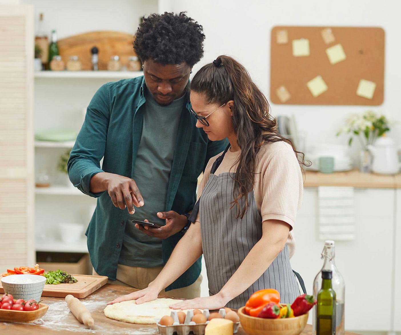 A couple references their phone as they make pizza together at home.