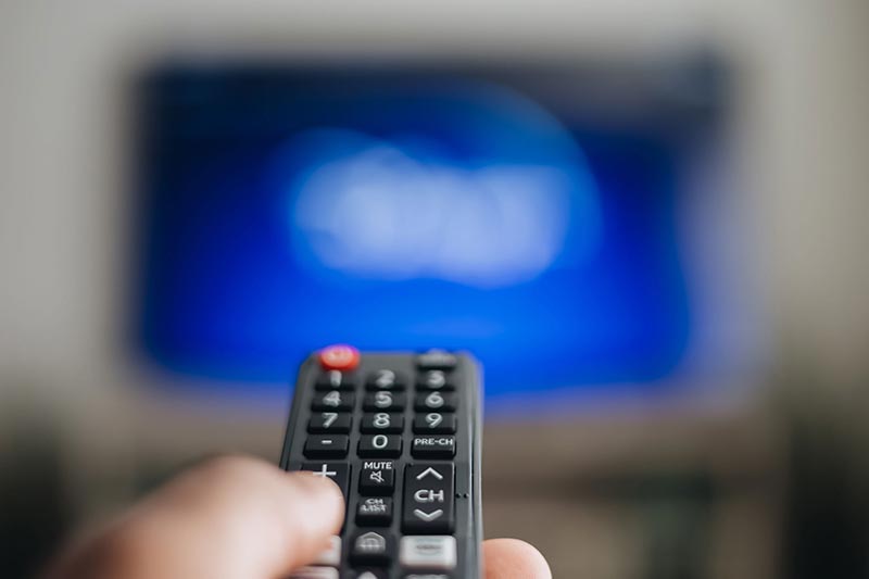 A remote control points at an out of focus television.