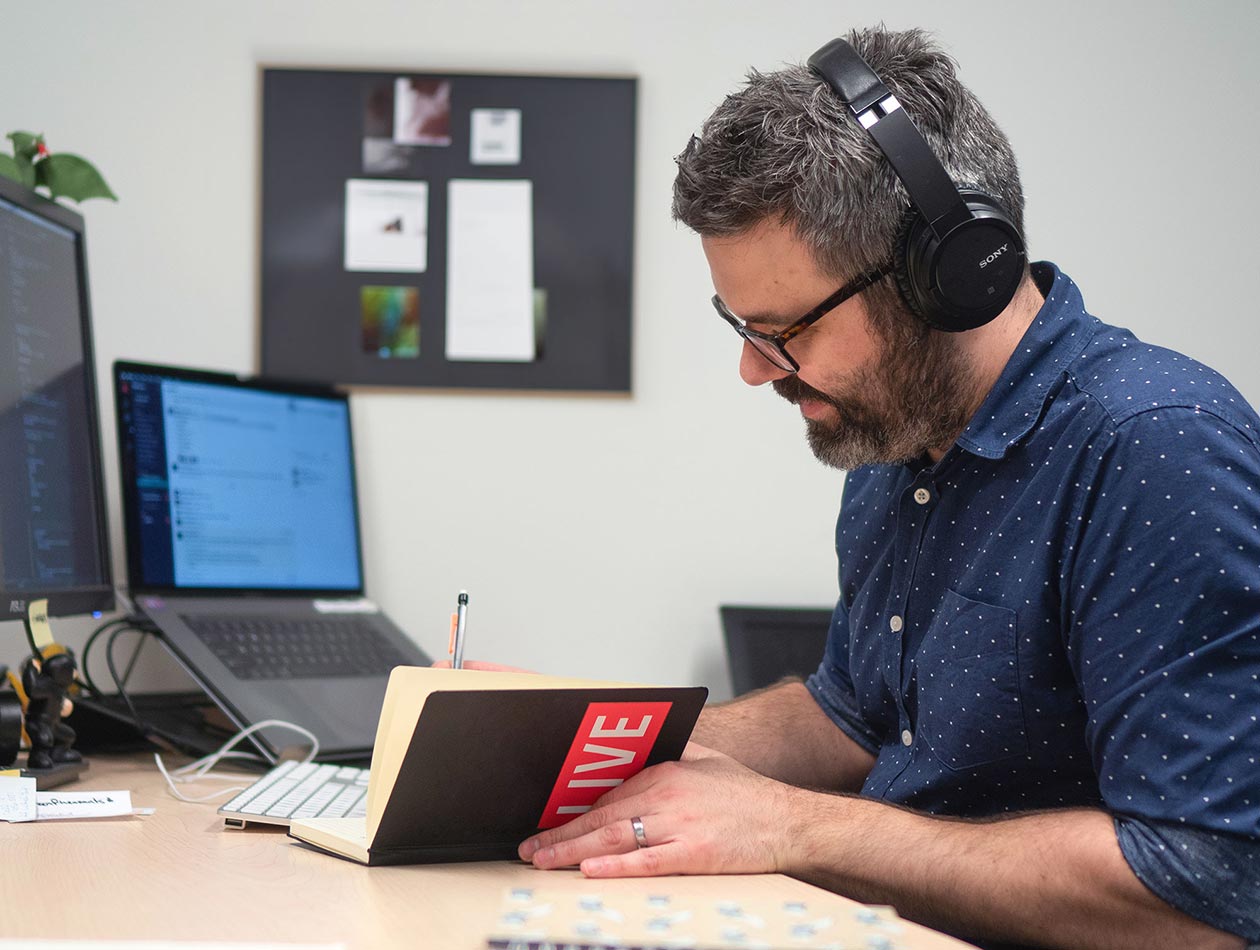 A developer writes notes in a notebook as he codes.