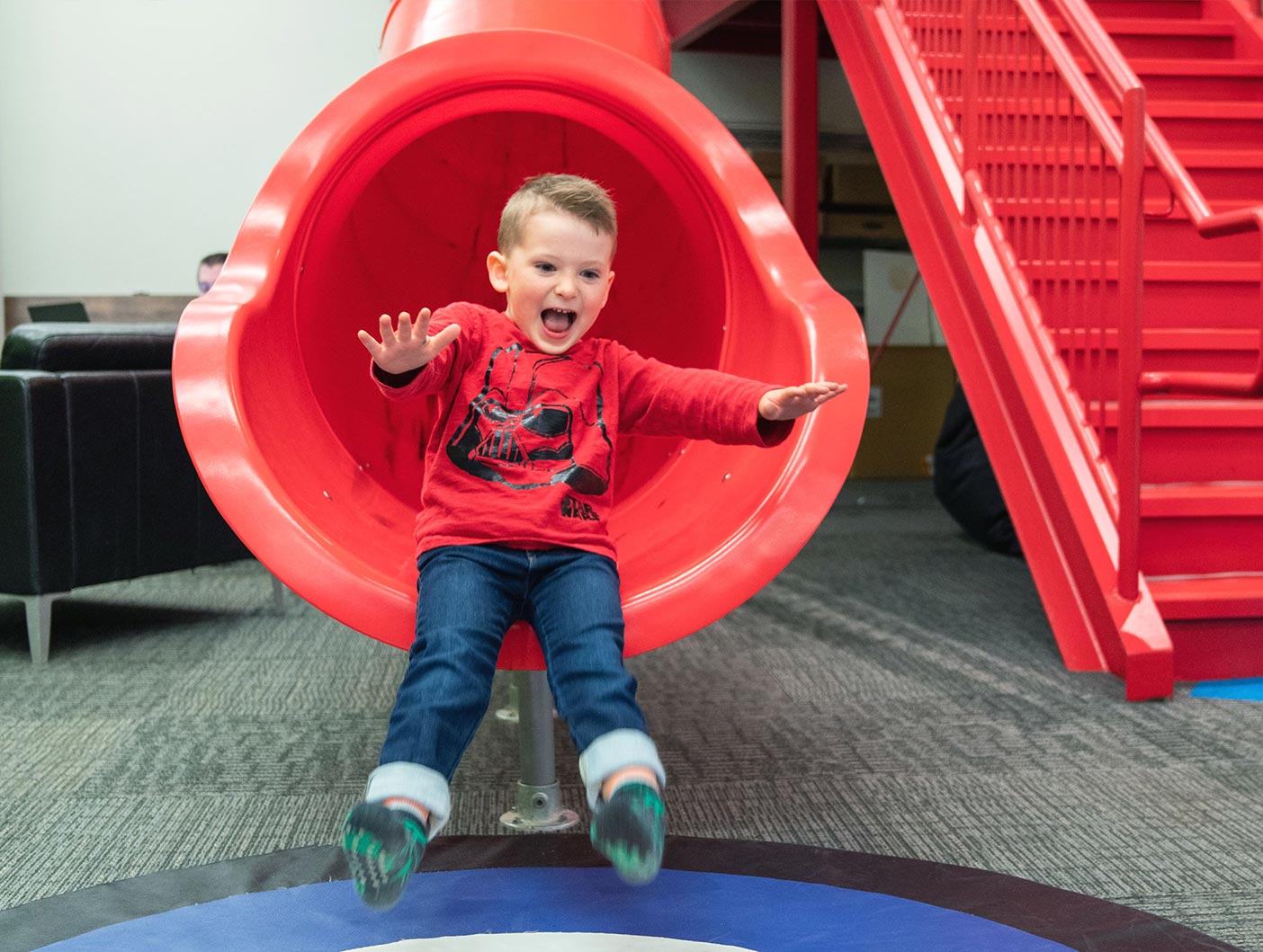 A small boy slides down a large red slide at the REDspace office.