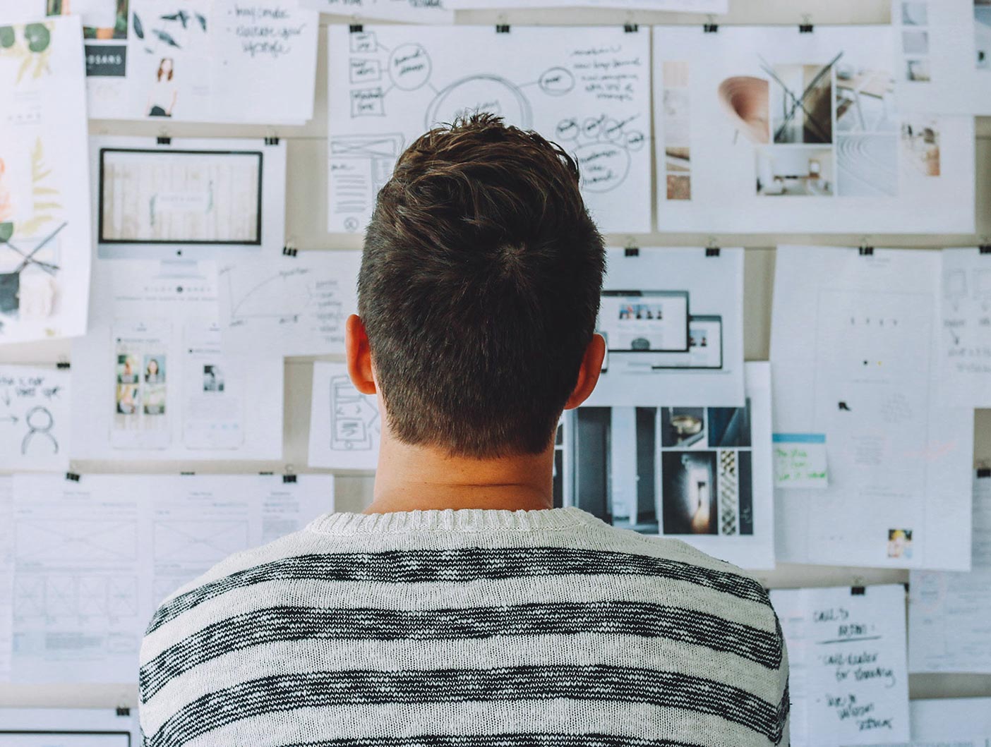 A designer looks over a whiteboard filled with ideas on paper.