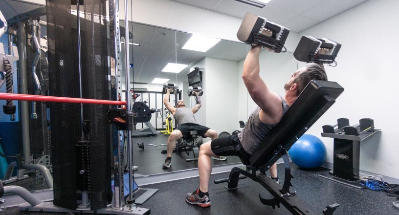 A young man lifts weights on an incline bench in the REDspace office gym.