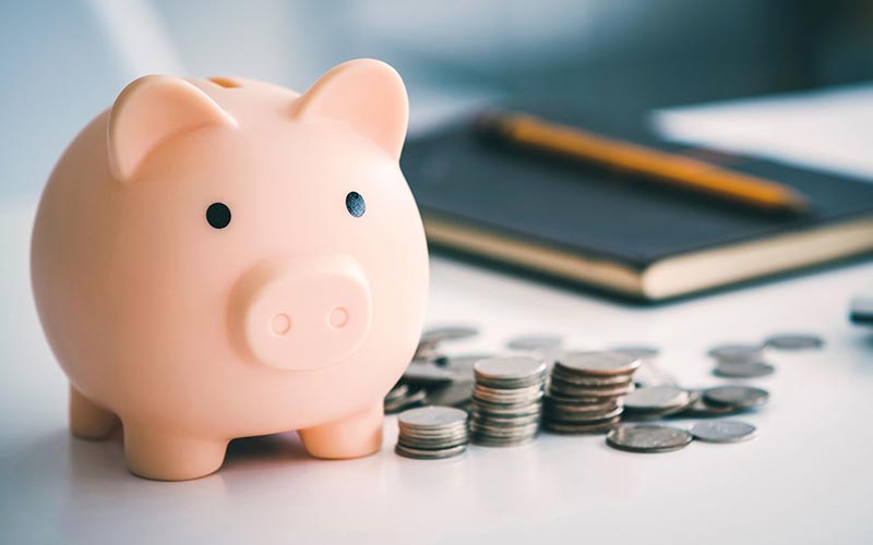 A piggy bank sits next to multiple stacks of coins.