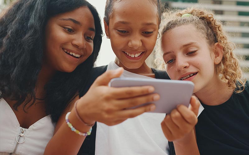 Three young girls gather around a phone to watch content.