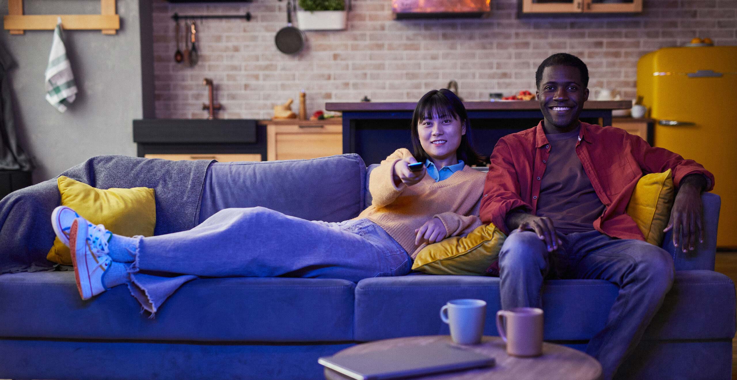 A young man and woman relax on a couch enjoying television.