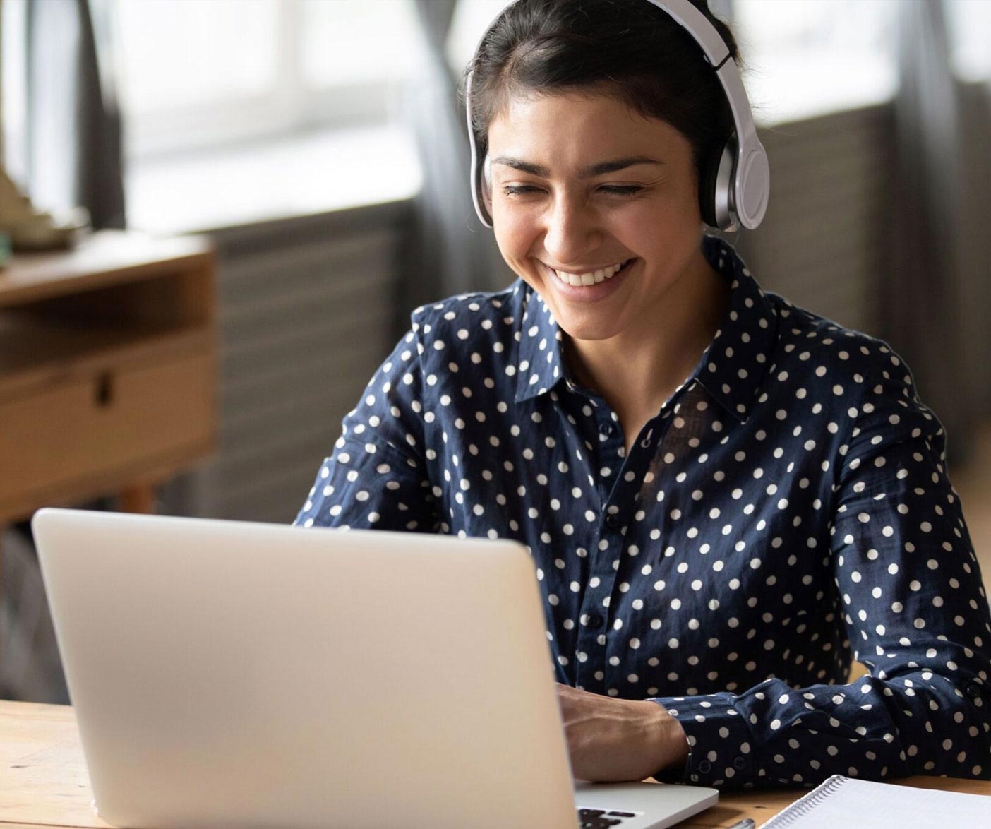A young woman wearing headphones smiles during a conference call on her laptop.