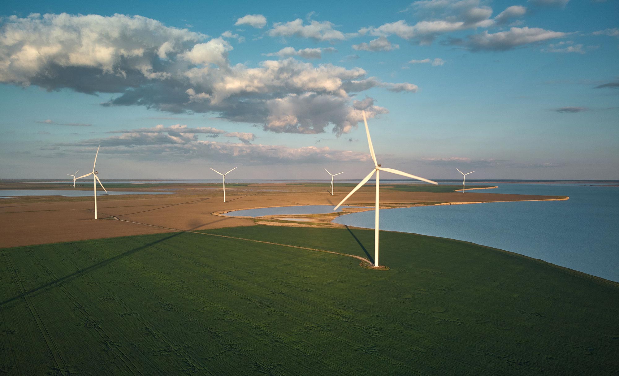 A field of wind turbines sits next to a large body of water.