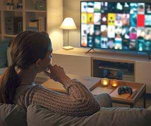 Woman sits on couch watching television.