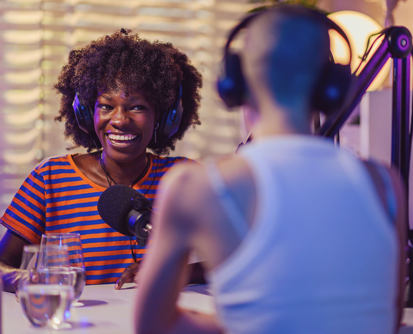 A woman wearing headphones talks with another person during a podcast recording.