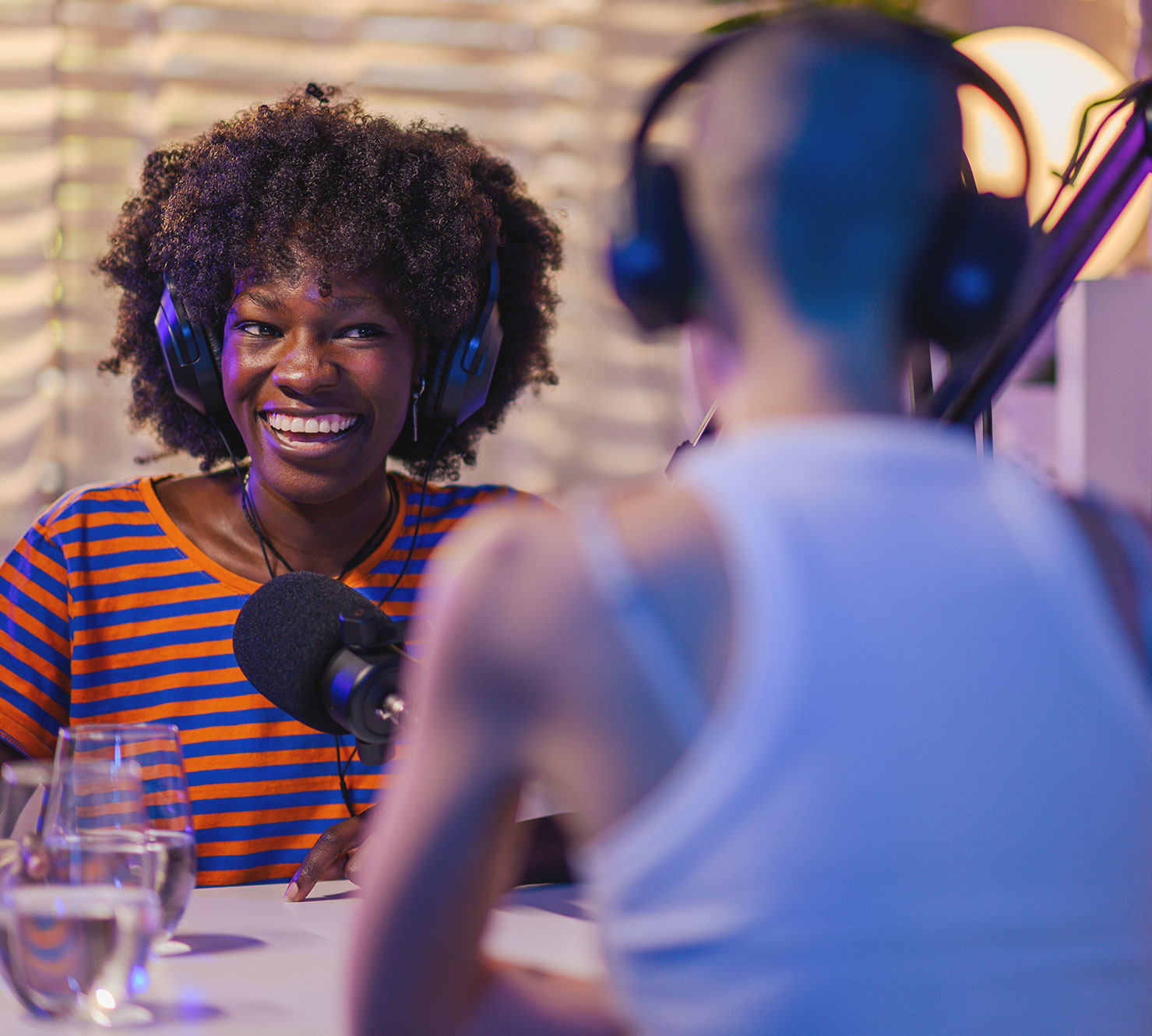 A woman wearing headphones talks with another person during a podcast recording.